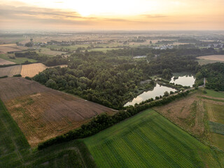 Malowniczy widok z drona na pola, las i stawy o zachodzie słońca. Wiejski krajobraz rolniczy w złotym świetle. Panorama polskiej wsi z lotu ptaka, natura i sielski spokój wieczorem. © Henryk Niestrój