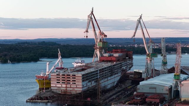 Aerial view of a shipyard where a large ship is under construction, surrounded by cranes and vessels, reflecting the industrial activity, Pula, Istria County, Croatia.