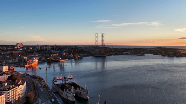 Aerial view of an industrial port with ships and an offshore platform, reflecting the soft sunset hues over the calm water, Pula, Istria County, Croatia.