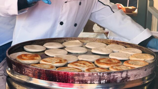 At the market, a chef carefully flips freshly made Xian Bing on a large round griddle. Chinese street food culture. High quality 4k footage