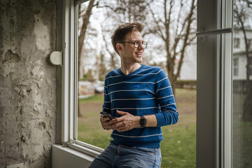 Young man using smart phone looking away by window