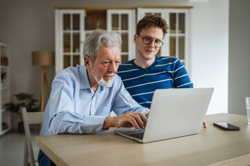 Fototapeta premium Young man teaching senior man using laptop at home