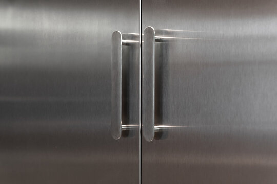 Stainless steel cabinet doors with modern oval handles. Close-up of sleek, metal double doors featuring minimalist silver handles - professional industrial design with clean lines.