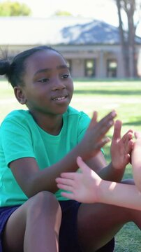 Vertical video: Reaching girl in teal tee placing hands on partner, playing hand-clap game on lawn