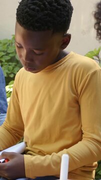 Vertical video: Taking marker from peer, pupil in mustard tee marking red folder for class on patio