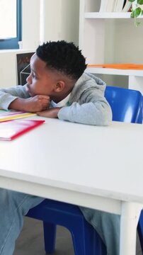 Vertical video: Reading striped notebook at desk, kid in hoodie turning pages then resting, gazing
