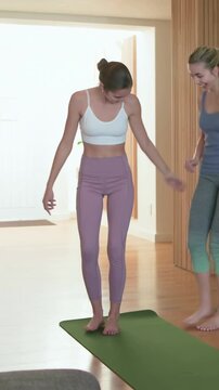 Vertical video: Starting woman white bra holding tree pose on green mat, friend helping for balance