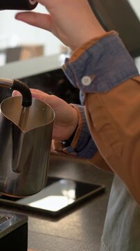 Vertical video: Order alert barista in green apron steaming milk in pitcher pulling shot at counter
