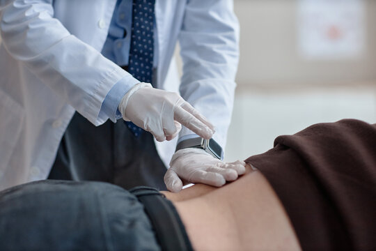 Urologist wearing gloves examining lower back of adult man in clinical setting, focusing on physical assessment for urological evaluation