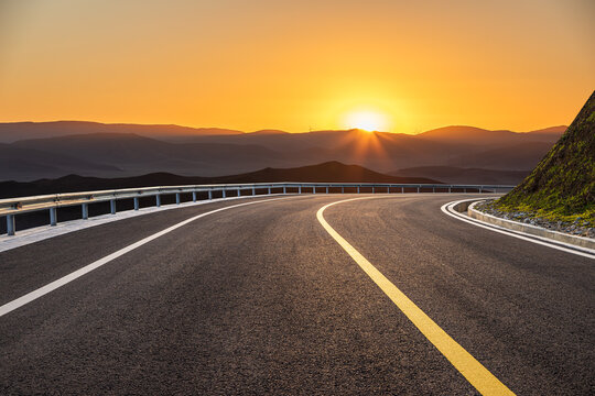 Winding asphalt highway through rolling hills under a golden sunset sky in the countryside.