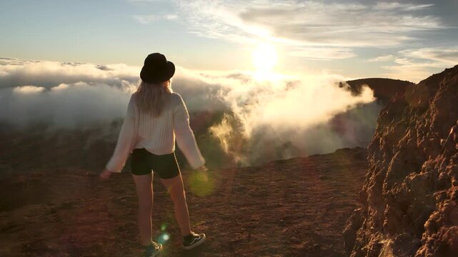 Beautiful girl standing at Mauna Kea summit, overlooking above the clouds at sunset. Highest mountain on the world. High quality 4k footage