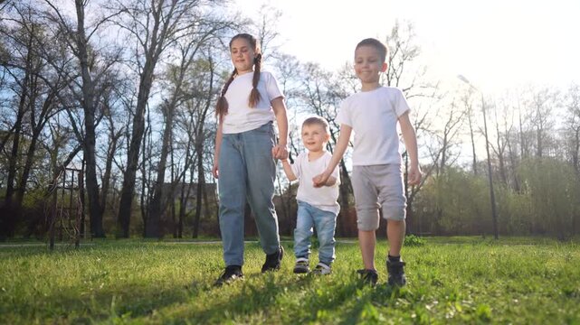 happy family. A family kid enjoys a summer walk in the park, with children brother sister holding their baby s hands as they step on the grass. happy family kid dream concept.