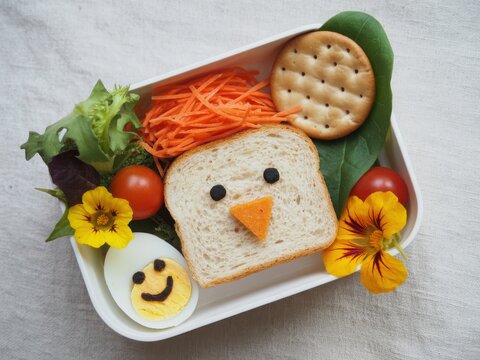 A creative and healthy bento box lunch featuring a cute bread face and colorful fresh vegetables