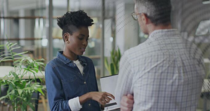 Vertical video: Facing man, woman in denim pointing at laptop explaining in office, glass partition