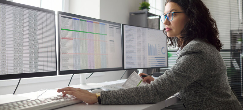 Accountant woman performs audit and analysis of finance. She reviews data on computer monitors in office, checks reports and spreadsheets for compliance. Core concept is audit accuracy.