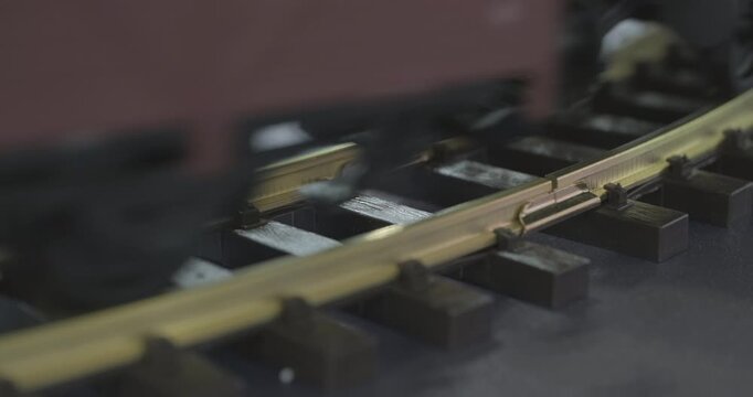 A miniature toy steam train is moving along the railway tracks, the locomotive is pulling several carriages.