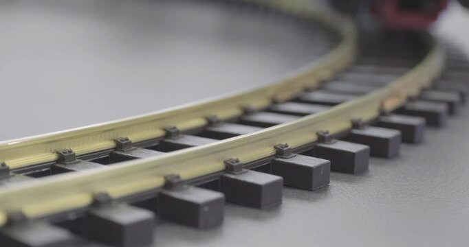 A miniature toy steam train is moving along the railway tracks, the locomotive is pulling several carriages.