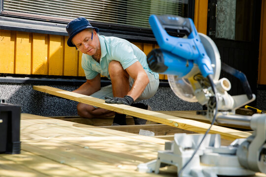 Man building wooden deck in backyard. Authentic DIY home improvement project during summer. Outdoor house renovation and construction.