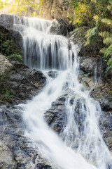 Obraz premium Peaceful waterfall cascading down dark rock in tranquil nature landscape. Fresh water stream flowing through lush green forest. Serene beautiful outdoor scene bringing calm refreshing emotion