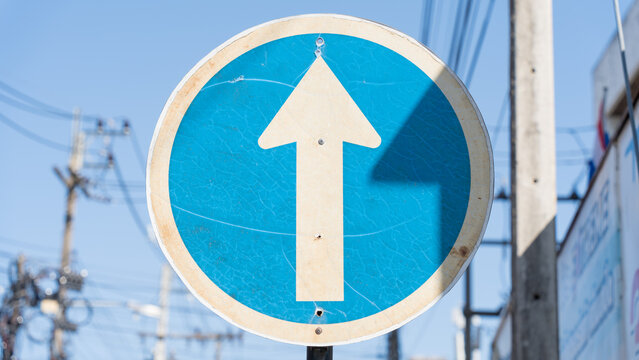 Blue circular one-way road sign with white arrow against clear sky