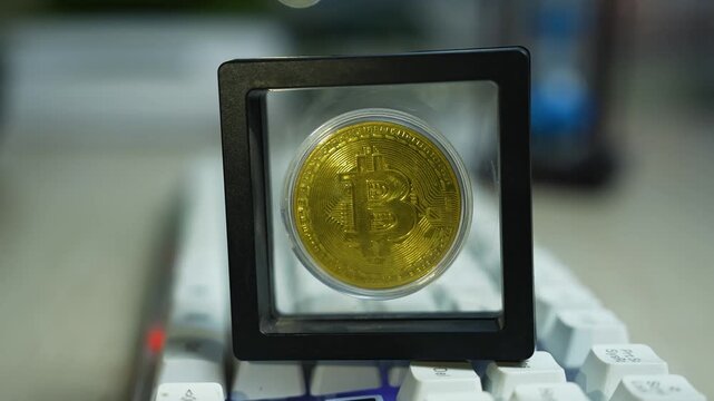 Gold bitcoin coin displayed in a clear square frame on top of a white keyboard
