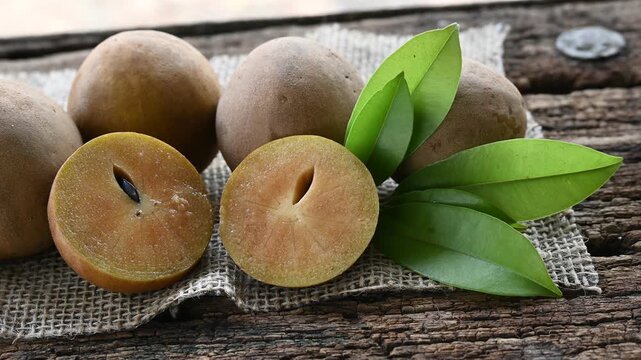 Fresh sapodilla (chikoo) fruit cut in half with green leaves on wooden backgrounds