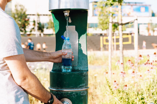 Man refilling plastic water bottle at public drinking fountain in city park