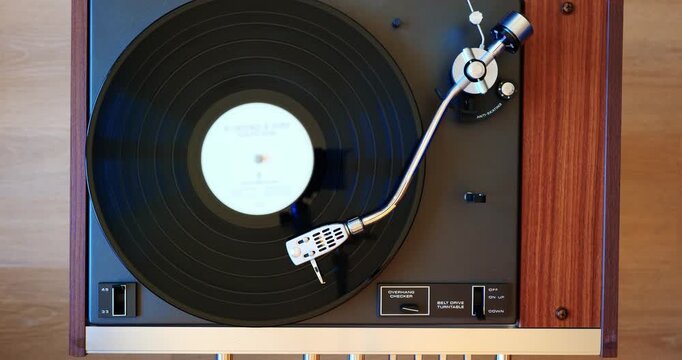 Vintage turntable with cantilever arm, stylus and a black vinyl record playing. Top down view, close up, real time video, no people