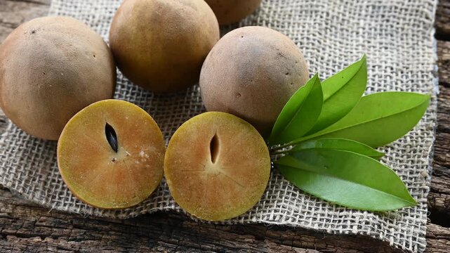 Fresh sapodilla (chikoo) fruit cut in half with green leaves on wooden backgrounds
