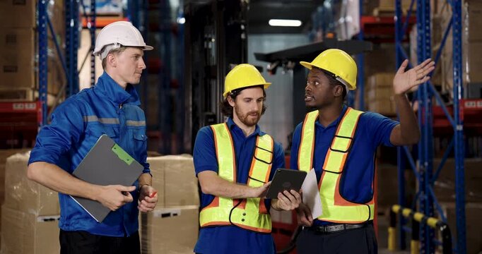 african american worker raising hand while discussing with caucasian supervisor and coworker near stacked pallet inside warehouse teamwork planning during inventory and logistic coordination task