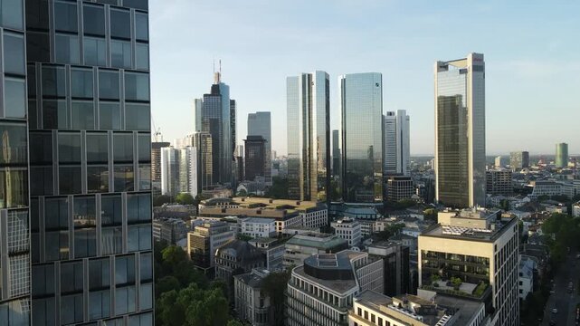 Drone rises along reflective skyscraper glass with Frankfurt skyline opening behind.