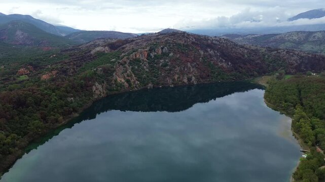 Cinematic drone pull-back shot revealing the stunning landscape of Lake Ziros in Preveza. High-angle view of mirror-like water and lush mountains. Perfect for nature and travel films.