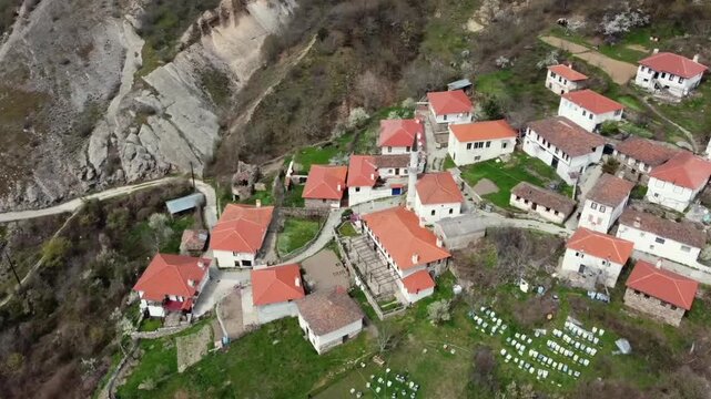Cinematic drone semi-orbit shot of the traditional Pomak village of Kottani. Detailed view of historic stone houses and red tiled roofs in the Rhodope mountains. Ideal for cultural documentaries.