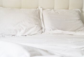 Obraz premium White bed with pillows and clean sheets on a simple headboard in a bright room