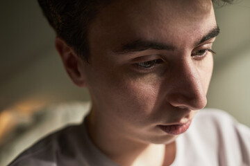 Obraz premium Portrait of Caucasian teenager boy looking down with serious expression, closeup showing thoughtful emotion, soft lighting highlighting facial features, background softly blurred
