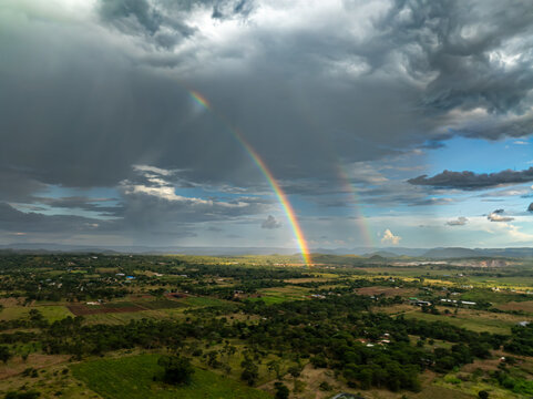 Aerial view of a vibrant rainbow arcing over the verdant landscape, contrasting with the brooding storm clouds, painting the sky with hope and drama, Chilanga, Lusaka Province, Zambia.