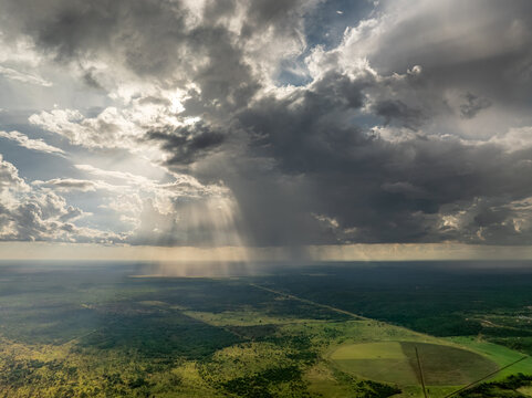Aerial view of sun rays piercing through dramatic clouds over a lush green landscape, creating a stunning contrast between light and shadow, Brazil.