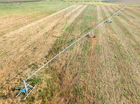 Aerial view of a center pivot irrigation system stretching across a field, contrasting golden stubble with patches of green, Chilanga, Lusaka Province, Zambia.