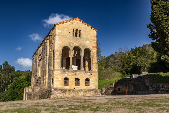 Fachada de Santa Mar&iacute;a del Naranco en Oviedo, Asturias. Monumento prerrom&aacute;nico del siglo IX, Patrimonio de la Humanidad, bajo un cielo azul con nubes en un entorno natural verde y soleado.