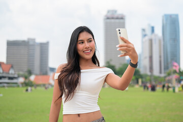 Cute woman smiling outdoors at Merdeka Square with Kuala Lumpur city skyline and a green park field
