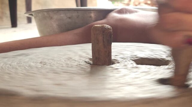 Close-up of a Indian woman using a traditional stone grinder to process grains or spices by hand. This authentic rural scene highlights Indian culture, handmade food preparation