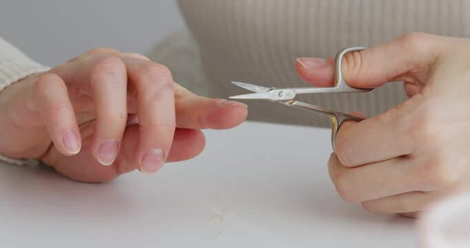 Female hands holding small scissors trimming and shaping fingernails for a manicure at home