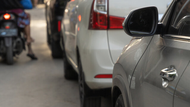 Close up of silver car side mirror and door handle in heavy city traffic with blurred white car and motorcycle background