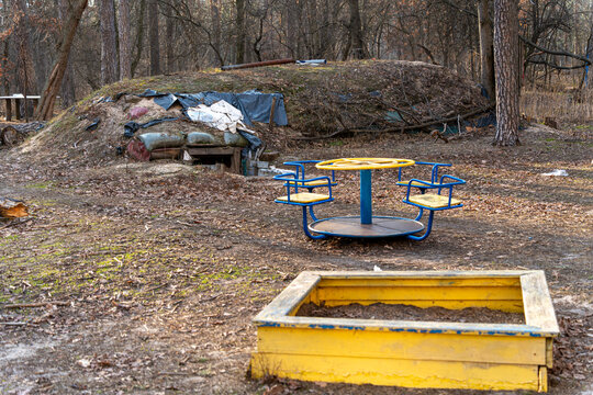 View of a playground with a yellow sandbox and carousel in the foreground and a camouflaged bunker lurking ominously in the background, Kyiv, Kyiv City, Ukraine.
