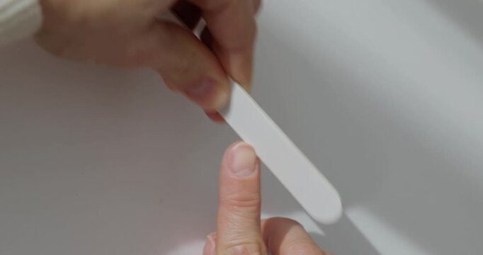 Closeup of a woman's hands using a nail file for a manicure at a white table
