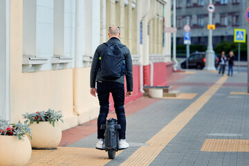 Motorized personal vehicle for efficient travel, man riding an electric unicycle on paved street with white sneakers and black clothing. Man balancing on an electric wheel, riding through city street © Tricky Shark