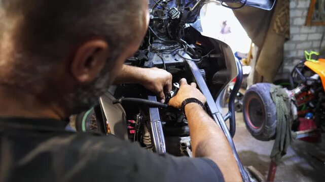 Professional mechanic repairing detail of motorcycle at workplace. Male repairer fixing engine of moto at workshop. Adult repairman mending vehicle motor at garage. Concept of maintenance service