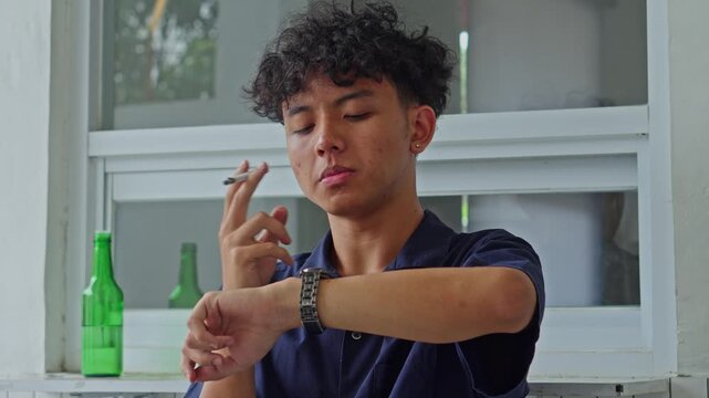 Casual portrait of young man smoking cigarette and checking time on wristwatch