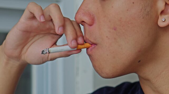 Close-up of young man exhaling thick smoke from burning cigarette