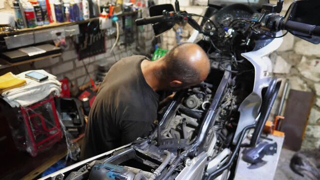 Adult repairman fixing motor of motorbike at workshop. Professional mechanic repairing engine of motorcycle at workplace. Male repairer mending detail of moto at garage. Concept of maintenance service